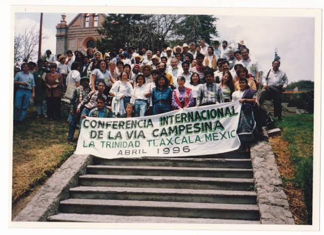 A história do MST sempre representou muita luta. O movimento, que foi formado em janeiro de 1984 a partir de uma união de trabalhadores rurais que convergiram no primeiro Encontro Nacional, realizado em Cascavel, no Paraná, é o resultado da grande necessidade de - no Brasil. Após o evento de janeiro de 84, foi realizado o primeiro Congresso do MST em janeiro de 1985, e dele as ideias de ocupação como forma de luta, junto dos princípios do movimento relacionados a luta pelas terras, reforma agrária e o socialismo começaram a ser idealizados.    Entre fracassos e sucessos, como o assentamento de 90 mil famílias graças ao Plano Nacional da Reforma Agrária, realizado em pequena escala em relação com a prévia inicial de 1,5 milhão, a realização do segundo Congresso do movimento, em Brasília, com a reafirmação das ocupações em pauta, o MST crescia em sua infraestrutura e dentro do âmbito político nacional.   Junto a isso, em 1993, foi criado a Via Campesina, um conjunto internacional que aglutinava organizações camponesas, pequenos agricultores, trabalhadores agrícolas e comunidades indígenas. A fundação oficial do grupo se deu em uma conferência internacional realizada em Mons, na Bélgica, com presença do MST, que era aliado desde antes da concepção da Via Campesina. Com esse conjunto operante, se abriram portas dentro do MST para dialogar com movimentos campesinos no mundo inteiro em prol de restaurar a soberania alimentar em países agredidos pelo imperialismo.    Mulheres Membras da Vía Campesina em Tlaxcala, México, em 1996. Reprodução: Capire  O MST começou a organizar brigadas internacionais, mas foi antes das brigadas e até antes da criação da Via Campesina que o MST possui essas relações e ambições internacionais. Conversamos sobre a história do Internacionalismo do movimento e sobre as brigadas com Judite Santos, membro da Coordenação Nacional e militante do MST. Para ela, o Movimento sem Terras nasceu como uma organização internacionalista, carregando heranças de lutas anteriores no Brasil e na América Latina