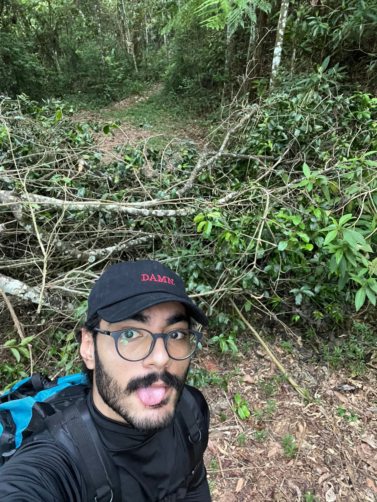 Montanhista posando à frente de um amontoado de galhos que bloqueiam a trilha